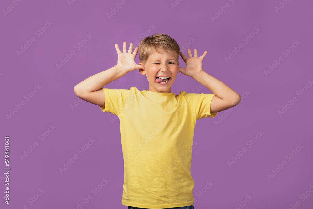 Young blond Caucasian kid preteen boy making faces staying against purple background. Studio shot. Young blond Caucasian kid preteen boy making faces staying against purple background. Studio shot.