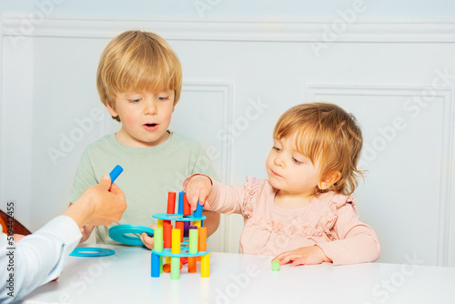 Cute boy and girl build with help of adult tower on the table