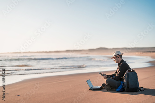 digital nomad sitting on the beach working with his laptop on the shore of the beach at sunset