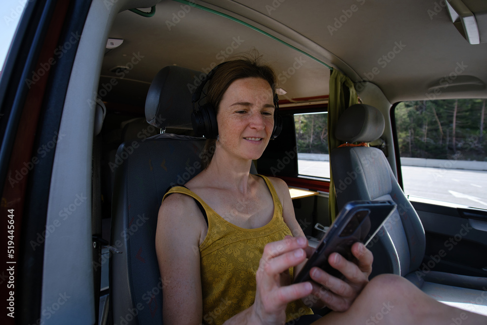 Woman in headphones browsing smartphone in automobile