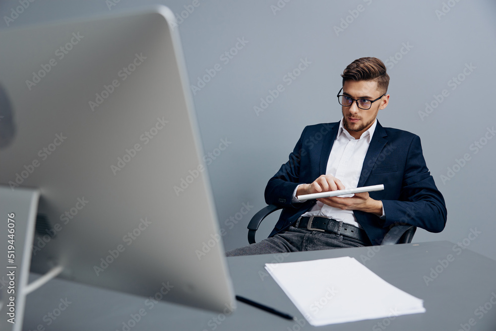 a man in a suit wearing glasses works in front of a computer Gray background a man in a suit wearing glasses works in front of a computer Gray background