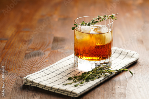 Obraz na plátně a tumbler glass with brown alcoholic drink, thyme and ice cubes on linen napkin
