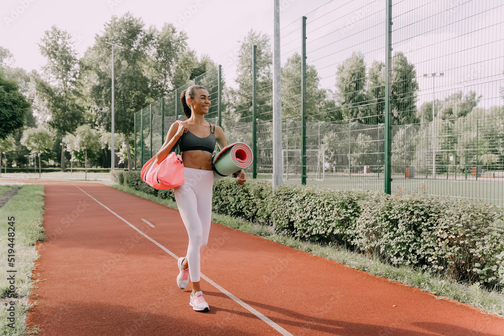 Young attractive African slim fit woman in sportswear preparing to go to workout with a training bag and mat in hand Young attractive African slim fit woman in sportswear preparing to go to workout with a training bag and mat in hand