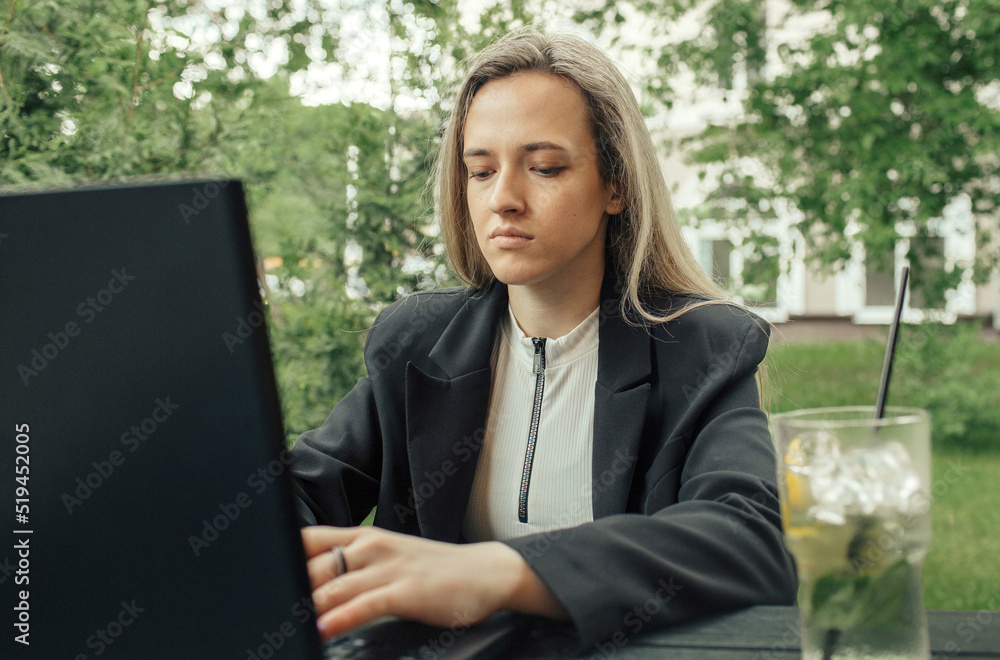 A business lady sits at a table in a summer cafe and works at a computer A business lady sits at a table in a summer cafe and works at a computer