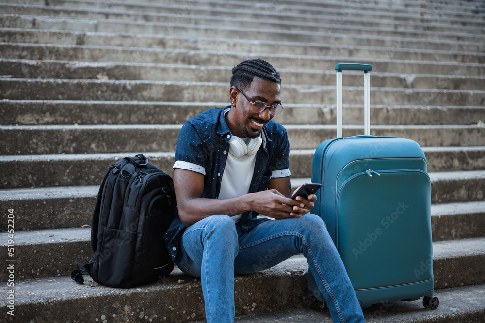 African man using his phone while he is sitting on stairs. He is waiting for the train to arrive.