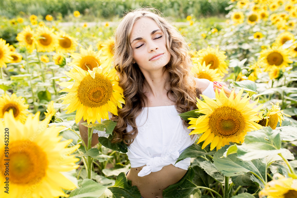 Young blonde girl with long curly hair in a field of sunflowers Young blonde girl with long curly hair in a field of sunflowers
