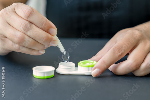 Woman takes contact lens out of container with tweezers. Black background, close-up, side view