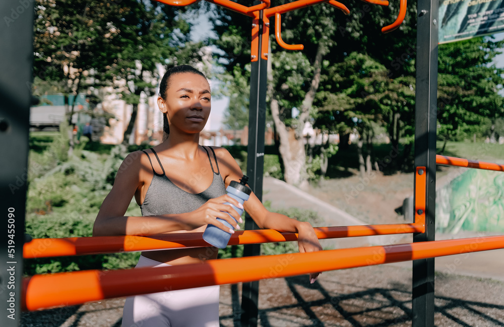 athletic African American woman on the playground with a bottle of water. Water balance concept
