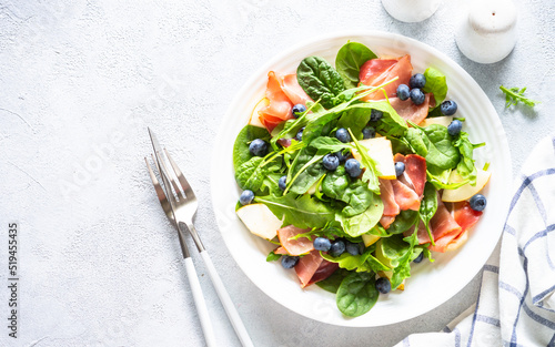 Healthy salad with spinach, jamon, pear and blueberry. Top view on white background with space for text.
