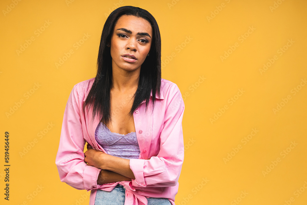 Obraz premium Displeased African american woman feels discomfort in stomach, keeps palms on tummy, has period cramps, wears casual t shirt, spoiled food, isolated on yellow background.