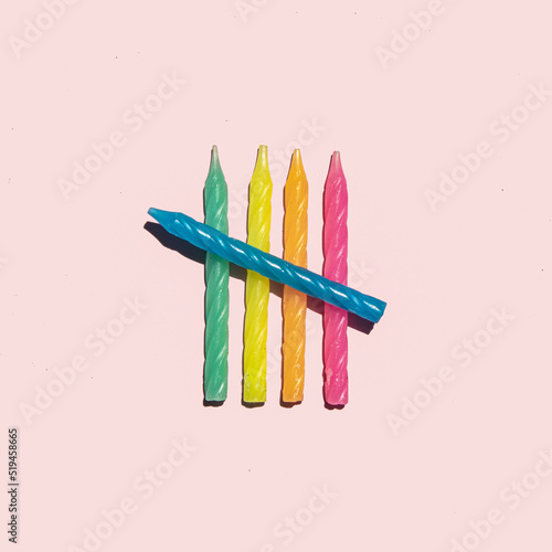 Colorful birthday candles on pastel light pink background. Symbolic party concept. Minimalistic celebration composition.