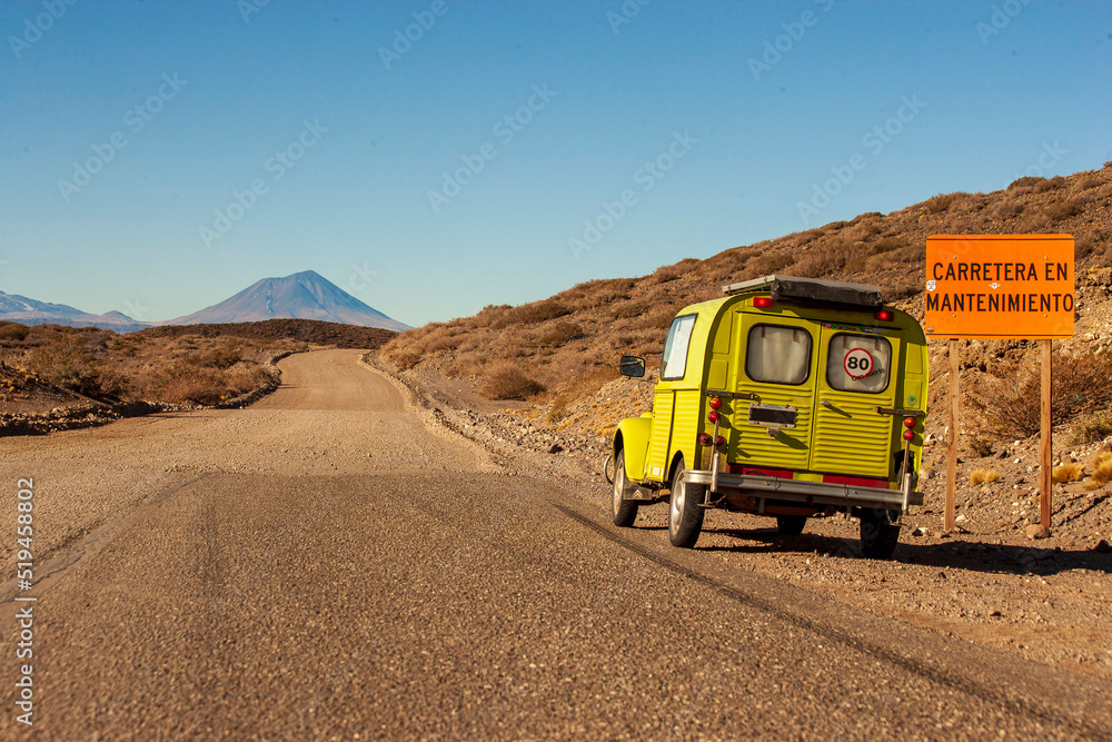 Old yellow car on the pavement road. The letters with CARRETERA EN MANTENIMIENTO mean CARRETERA EN MANTENIMIENTO