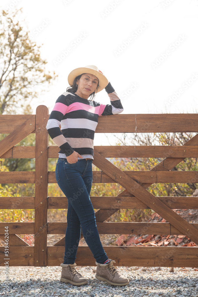 mujer sola con sombrero reposando en tranquera de madera mujer sola con sombrero reposando en tranquera de madera