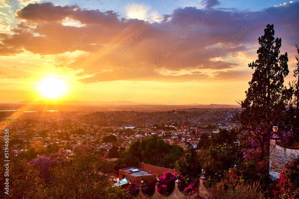 Fototapeta premium sunset in city with sun in the horizont with yellow colors and purpple clouds and sunshines in san miguel de allende guanajuato