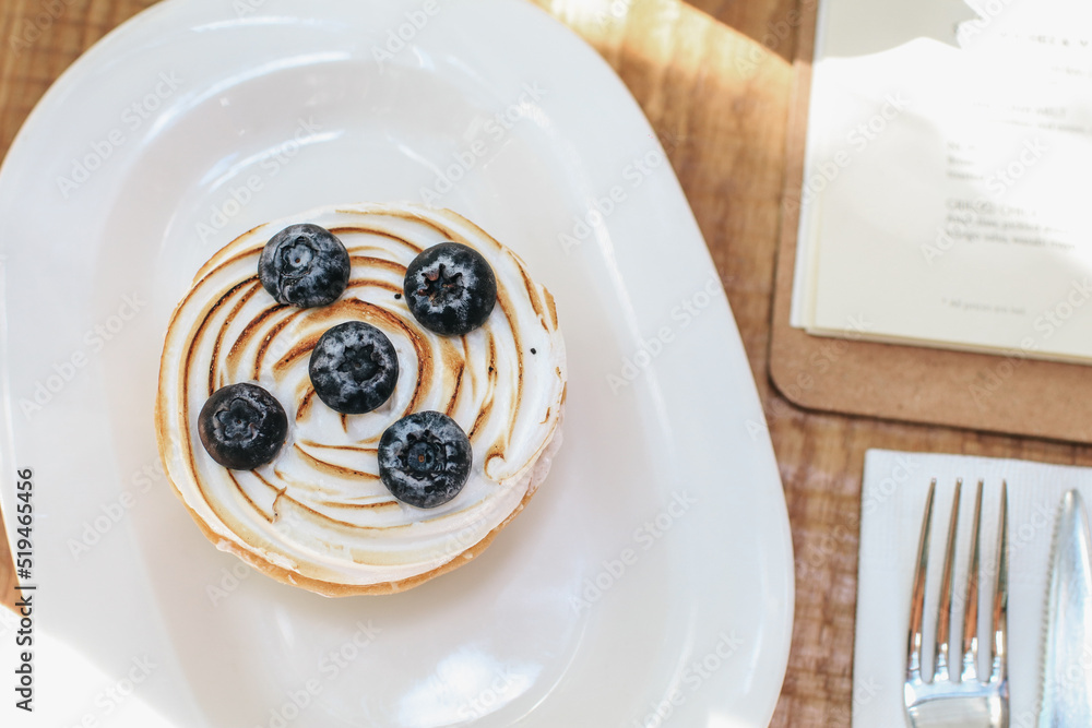 Lemon meringue and blueberry tart in white plate on wooden table. Pie Dessert. Horizontal Copy space - obrazy, fototapety, plakaty 