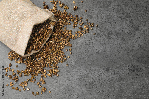 Overturned sack of gold nuggets on grey table, flat lay. Space for text photo