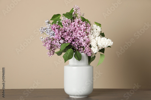 Wallpaper Mural Beautiful lilac flowers in vase on wooden table against beige background Torontodigital.ca