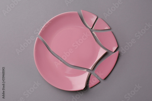 Pieces of broken pink ceramic plate on grey background, top view