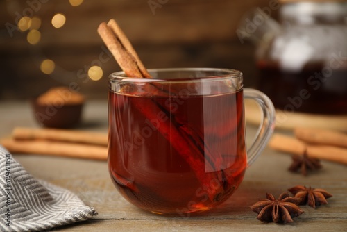 Glass cup of hot tea with aromatic cinnamon on wooden table against blurred lights