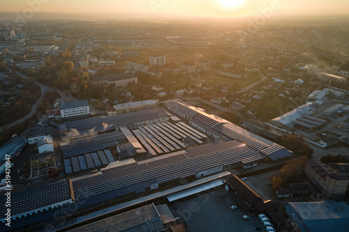 Aerial view of solar power plant with blue photovoltaic panels mounted on industrial building roof for producing green ecological electricity. Production of sustainable energy concept