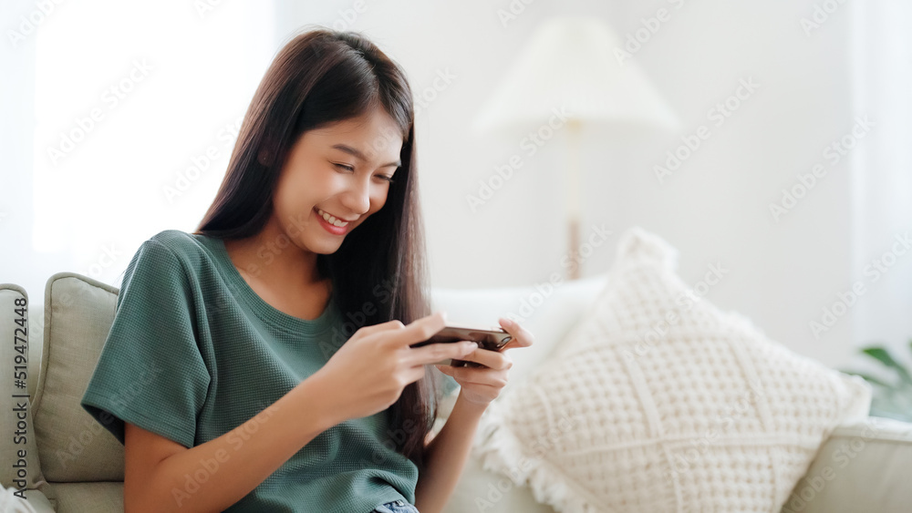 Happy young asian woman relax on comfortable couch at home texting messaging on smartphone, smiling girl use cellphone chatting, browse wireless internet on gadget, shopping online from home Happy young asian woman relax on comfortable couch at home texting messaging on smartphone, smiling girl use cellphone chatting, browse wireless internet on gadget, shopping online from home
