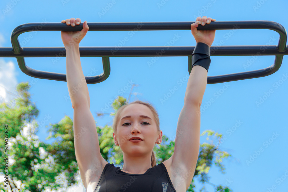 Fototapeta premium Young blonde woman in a dark tracksuit is engaged in fitness on the sports ground