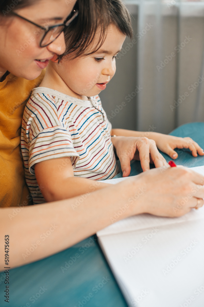 Mom with her boy are drawing with a pencils sitting at a table at home. Writing education concept. Mom with her boy are drawing with a pencils sitting at a table at home. Writing education concept.
