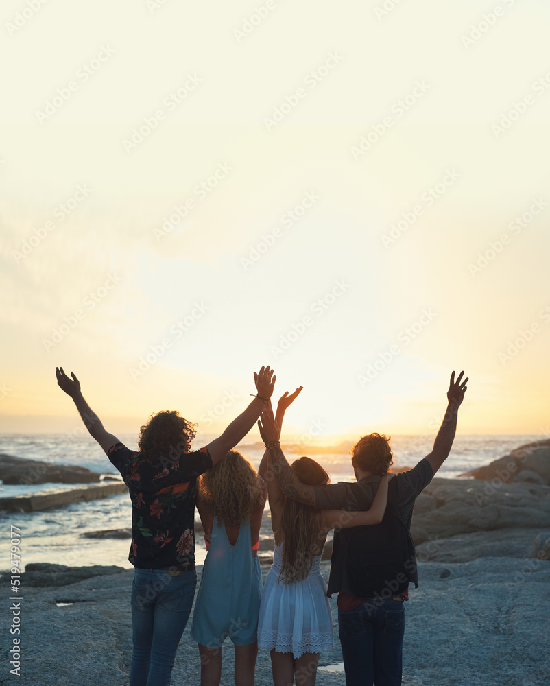 group of friends celebrating arms raised on beach looking at beautiful sunset enjoying summer vacation lifestyle