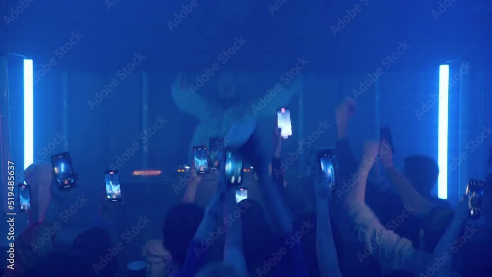 A crowd of people dancing on the dance floor of a nightclub under the light of colored spotlights. People are shooting videos on their smartphones. Night club A crowd of people dancing on the dance floor of a nightclub under the light of colored spotlights. People are shooting videos on their smartphones. Night club