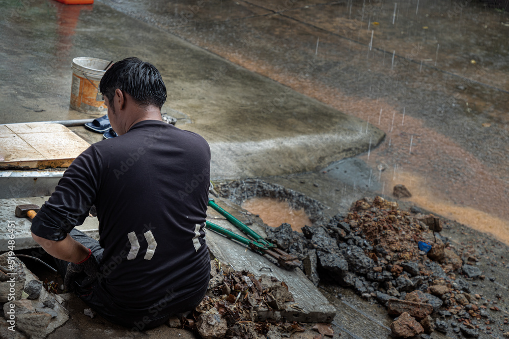 Utility workers using tool to fixing broken water main for commercial building water supplies during a rain. Plumbing problems. Focus and blur. Utility workers using tool to fixing broken water main for commercial building water supplies during a rain. Plumbing problems. Focus and blur.