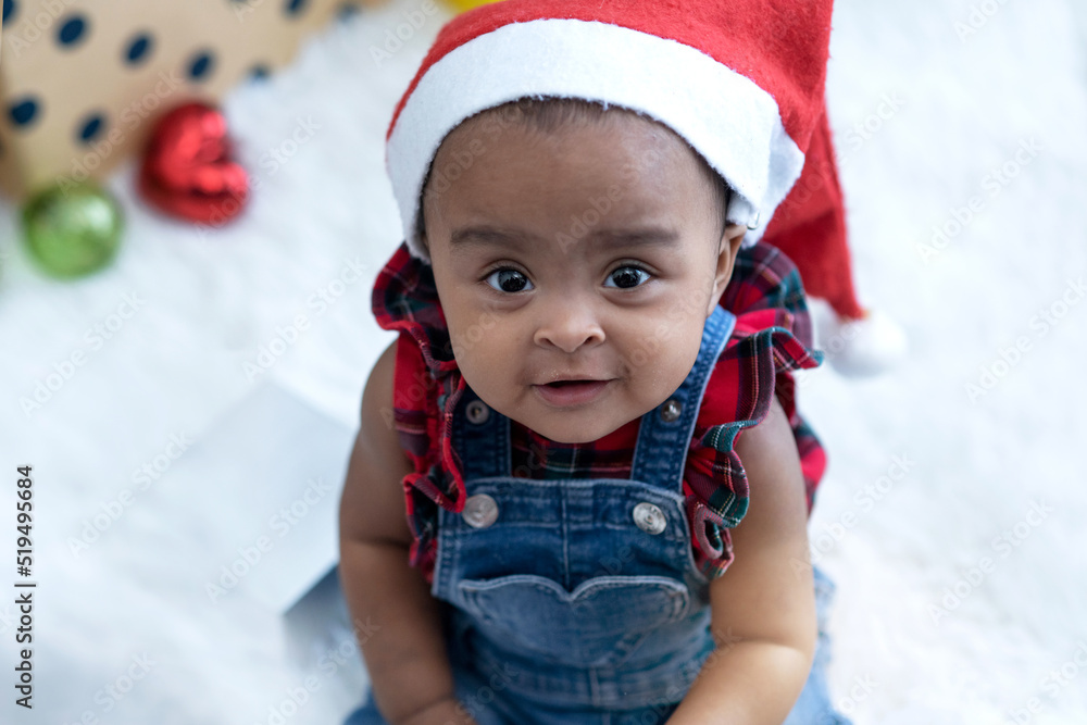 African American baby girl wearing Santa hat sitting on fur in room, Christmas time, Holiday season, looking at camera African American baby girl wearing Santa hat sitting on fur in room, Christmas time, Holiday season, looking at camera