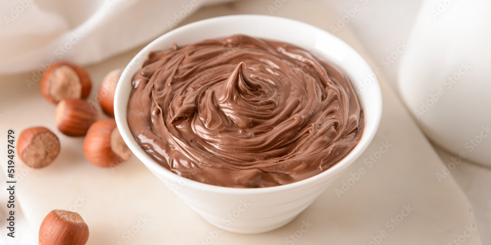 Bowl with tasty chocolate paste and hazelnuts on light table, closeup Bowl with tasty chocolate paste and hazelnuts on light table, closeup