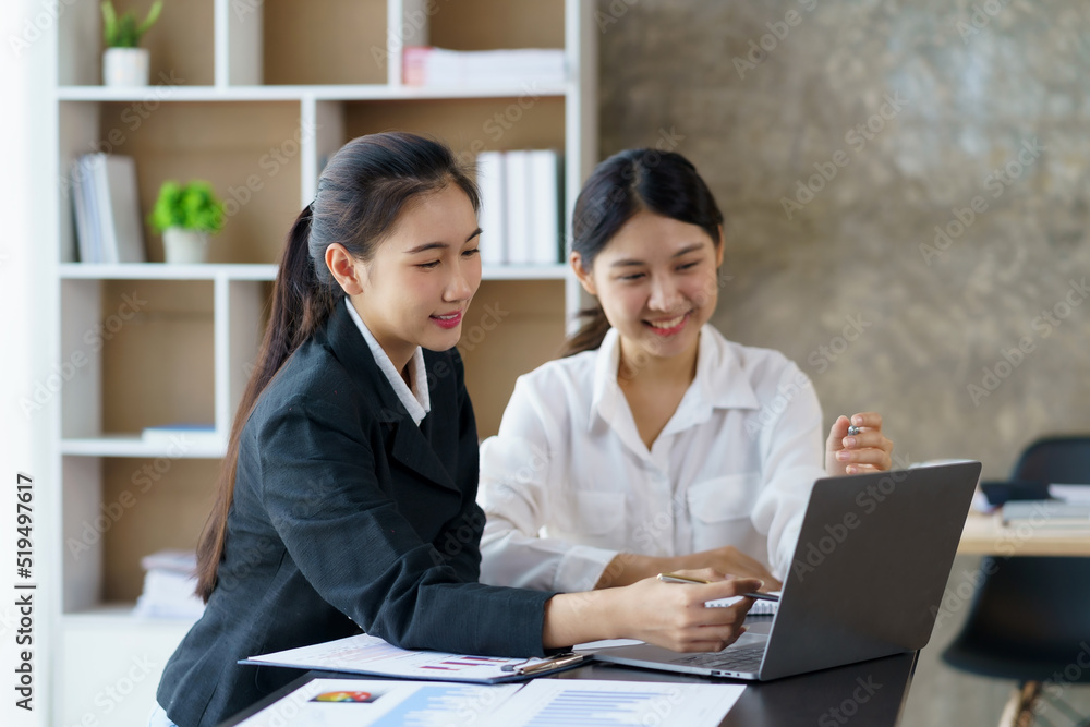 Two professional Asian business women discuss work using a laptop computer to work in the office. Two professional Asian business women discuss work using a laptop computer to work in the office.