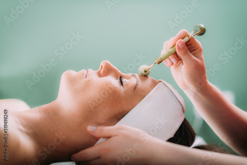 Guasha face massage in beauty salon, massage technique for stimulating pressure points on the face, using jade stone roller © Microgen