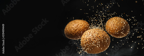 Flying burger buns with sesame seeds on black background with space for text photo