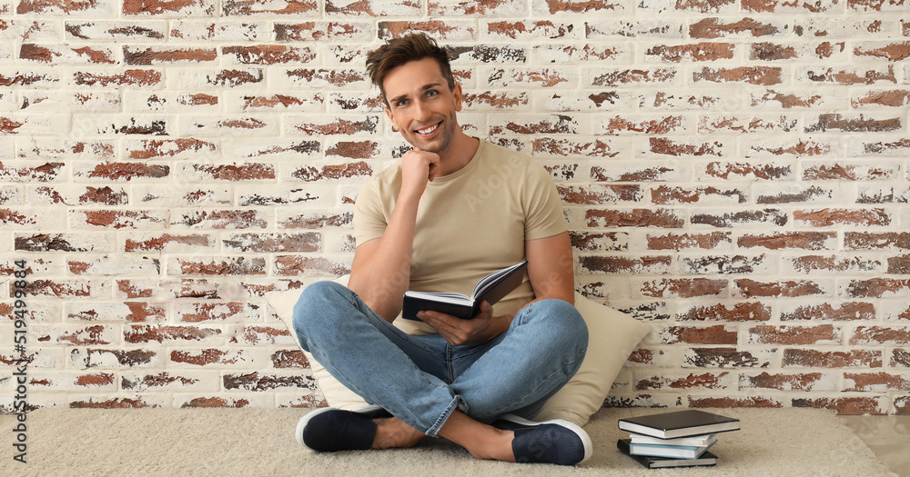 Handsome young man with books sitting near brick wall