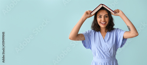 Beautiful funny young woman holding book on light blue background with space for text