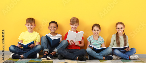 Cute little children reading books on yellow background