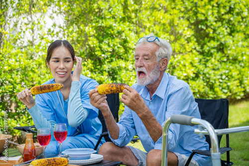 Elderly caregiver with man having fun while having lunch in the garden at home.