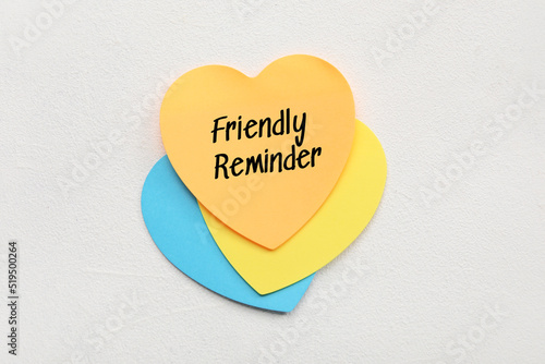 Heart shaped sticky note with text FRIENDLY REMINDER on light background photo