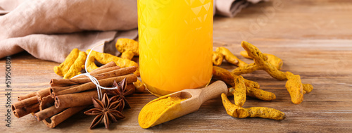 Glass of healthy turmeric drink with spices on wooden background