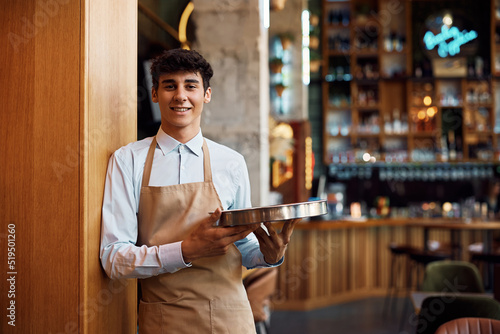 Bild auf Leinwand Young happy waiter working in cafe and looking at camera.