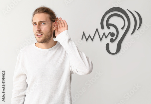 Young man with hearing problem on light background photo