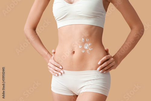 Young tanned woman with applied sunscreen cream on beige background