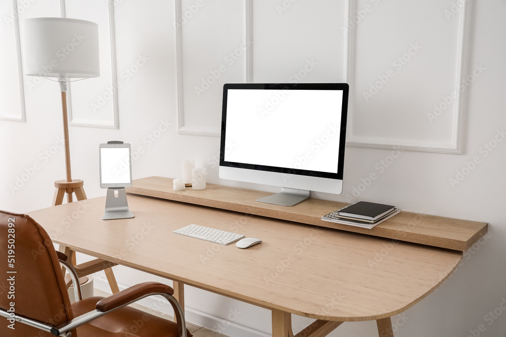 Modern workplace with computer and tablet near light wall Modern workplace with computer and tablet near light wall