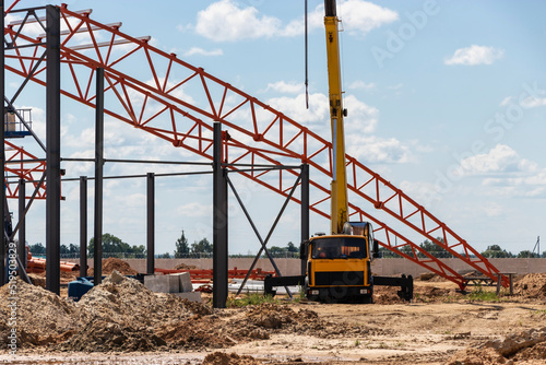 Installation of metal trusses and frame during the construction of an industrial building or factory. The work of installers during the installation of the roof. Construction of a large frame shop.