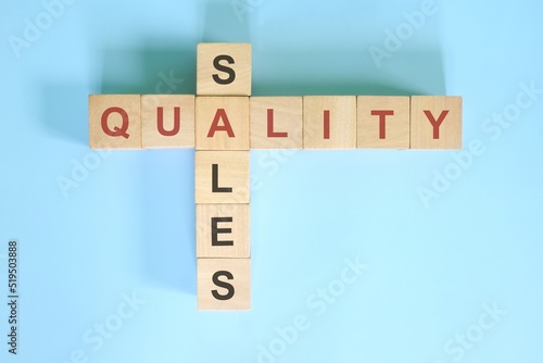 Obraz na płótnie High quality equals higher sales concept in business. Wooden block crossword puzzle flat lay in blue background. w salonie
