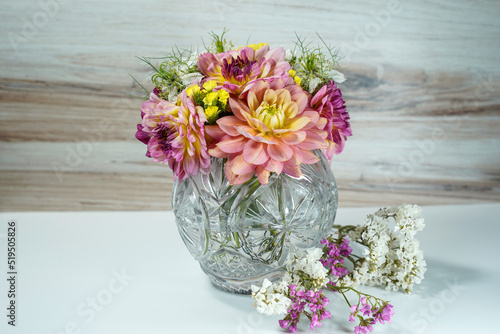 Wallpaper Mural Round glass bowl filled with a bouquet of dahlia and statice flowers. Pink, purple, yellow, and white flowers.  White table with wood background. Torontodigital.ca