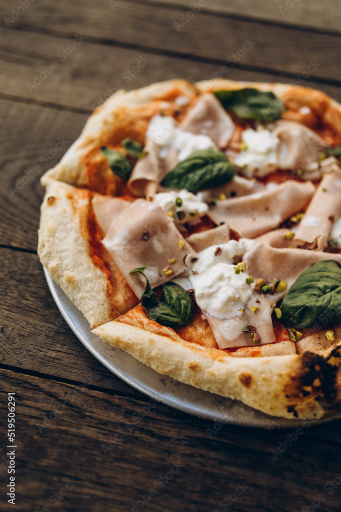 italian pizza with burnt sides on a wooden background top view. pizza with sausage, basil leaves, mozzarella and pistachios. sliced pizza close-up italian pizza with burnt sides on a wooden background top view. pizza with sausage, basil leaves, mozzarella and pistachios. sliced pizza close-up