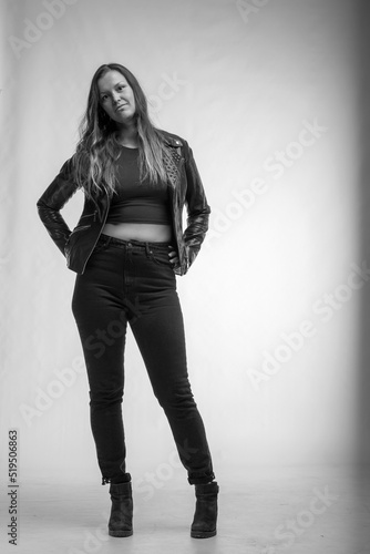 Woman in leather jacket and jeans standing on grey background in black and white